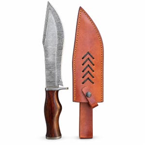 Op de afbeelding: Een vaststaand mes met een patroon van Damascusstaal en een voorgevormd donkerbruin houten handvat, vergezeld van een lichtbruine lederen schede met zwarte chevron-stiksels en een metalen drukknoopsluiting aan de voorzijde.