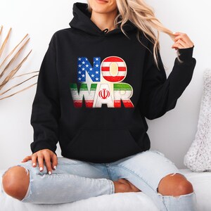May include: Black hooded sweatshirt with the words "NO WAR" in a colorful design. The "NO" is in the colors of the American flag, and the "WAR" is in the colors of the Iranian flag. A comfortable, casual top.