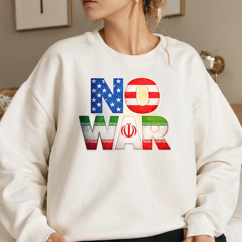 May include: White sweatshirt with the words "NO WAR" in a patriotic design. The "NO" is in the colors of the American flag, and the "WAR" is in the colors of the Iranian flag. A statement piece.