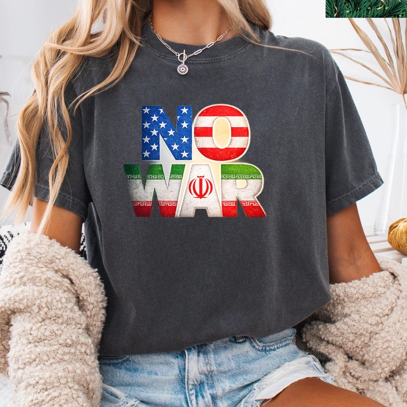 May include: Dark gray t-shirt with the words "NO WAR" in a distressed font. The letters are filled with the American and Iranian flags. The shirt is a casual style, suitable for everyday wear.