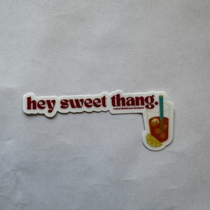 May include: A white sticker with red text that reads "hey sweet thang." A graphic of a drink with ice, a straw, and a lemon slice is on the right. The sticker also includes the text "charliebloom designs."