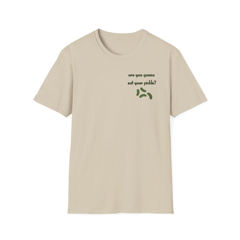 Peut inclure: T-shirt beige avec l'inscription "are you gonna eat your pickle ?" en noir et un motif de cornichons verts. Le t-shirt est &agrave; col rond et &agrave; manches courtes.