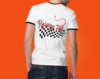 May include: White t-shirt with black trim featuring the text "Raising Hell" in red script with a devil tail design and a checkered flag graphic. The shirt is worn by a person wearing blue jeans.