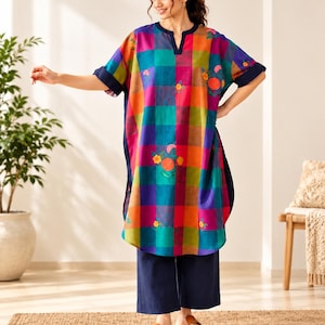 May include: A knee-length tunic featuring a vibrant multicolored plaid pattern in shades of orange, purple, teal, and pink, accented with small floral embroidery. The tunic has a navy blue notched neckline, cuffed sleeves, and is paired with solid navy blue wide-leg trousers.