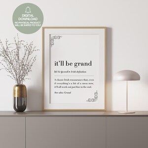 以下が含まれることがあります： 「it'll be grand」というフレーズが黒いテキストで書かれた、アイルランドの定義が書かれた額入りのプリント。プリントは金のフレームに入っており、花瓶とランプのある灰色の表面に表示されています。