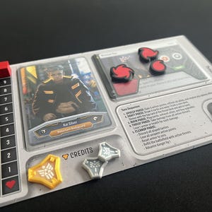 May include: A board game component with a card featuring "Kai Silver" and "Reluctant Bodyguard" text. Includes red, yellow, and gray game pieces, a discard pile, and a turn sequence section.