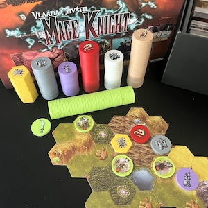 Puede incluir: Un juego de mesa "Mage Knight" con fichas de colores (amarillo, gris, morado, rojo, blanco, beige) y losetas hexagonales. Las losetas son principalmente marrones, amarillas y verdes.