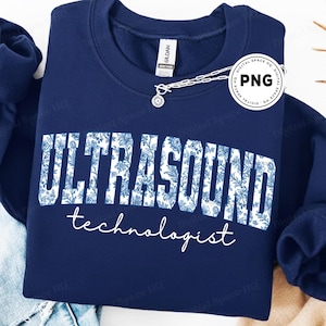 Puede incluir: Sudadera azul marino con las palabras "ULTRASOUND technologist" en blanco y azul floral. La sudadera es de la marca Gildan y tiene cuello redondo. Una cadena plateada con un colgante está sobre la parte superior.