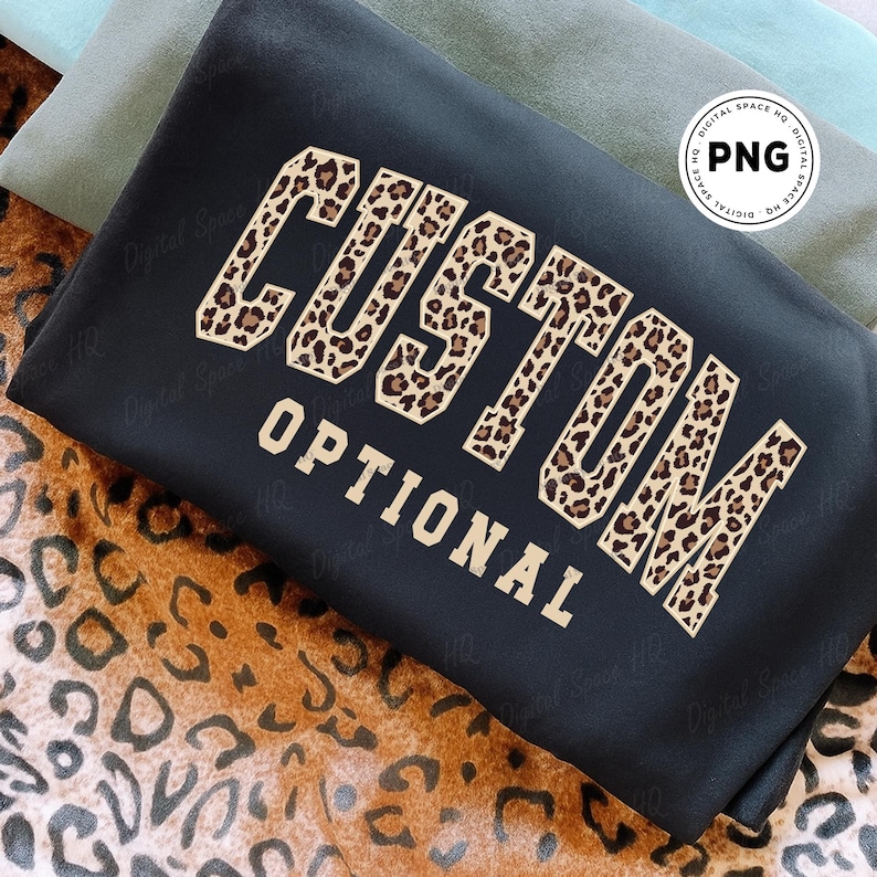 May include: Black sweatshirt with the word "CUSTOM" in a leopard print design, and the word "OPTIONAL" in a tan font. The sweatshirt is folded and placed on a leopard print surface.