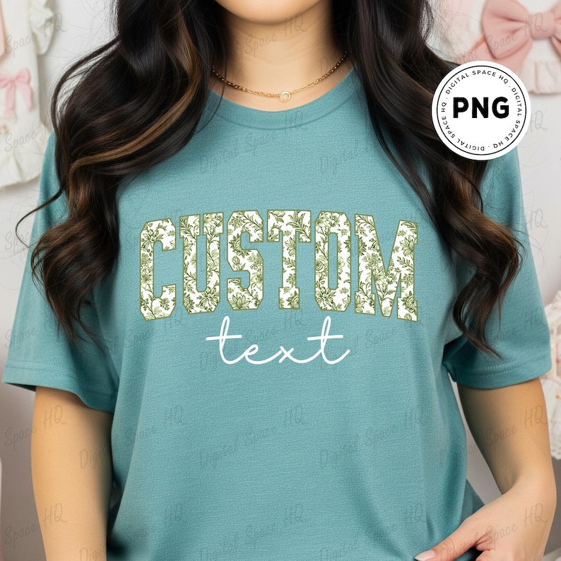 May include: Teal-colored t-shirt with the word "CUSTOM" in a floral design and the word "text" in a cursive font. The shirt is a solid color and has short sleeves.