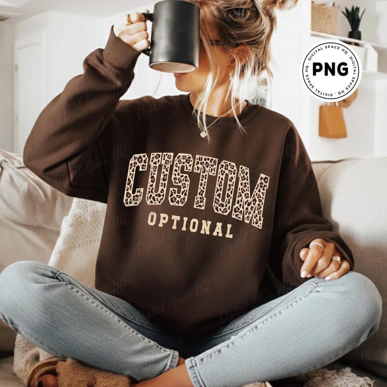May include: A brown sweatshirt with the words "CUSTOM OPTIONAL" in a leopard print design. The sweatshirt is a solid brown color. The image shows a person wearing the sweatshirt.