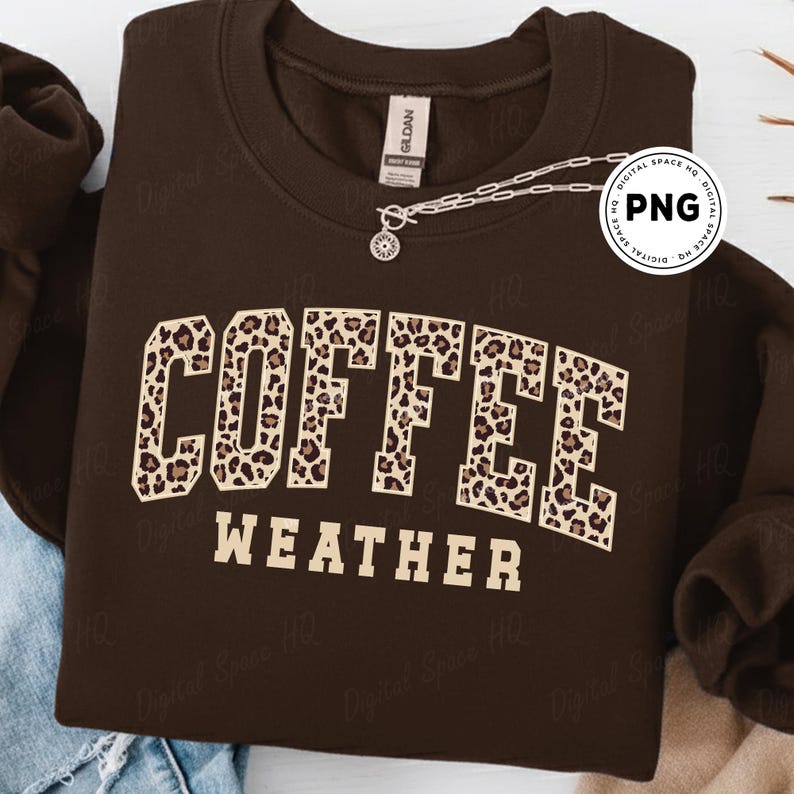 May include: A dark brown sweatshirt with the words "COFFEE WEATHER" in a tan, leopard print font. A silver necklace with a small pendant is draped across the top of the sweatshirt.