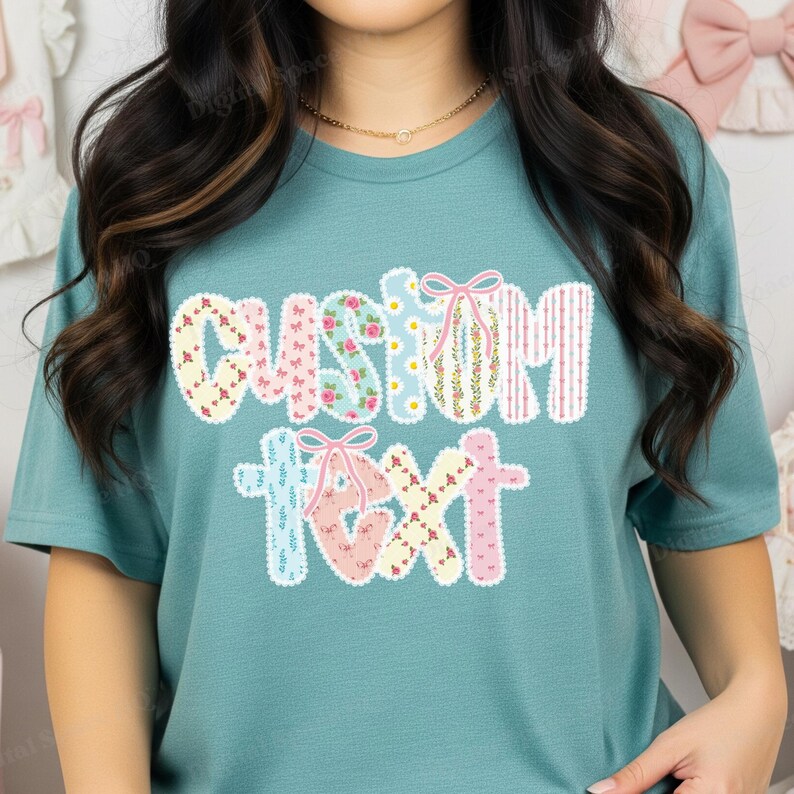 May include: Teal t-shirt with the words "CUSTOM TEXT" in a decorative, floral-patterned design. The letters are adorned with bows and various patterns, including floral prints and stripes. The shirt is a solid teal color.