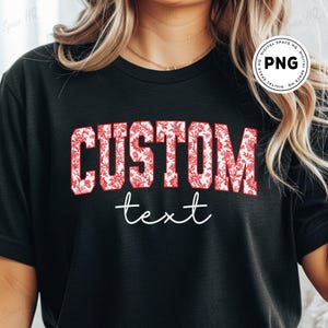May include: Black t-shirt featuring the word "CUSTOM" in a bold, red floral design font. Below, the word "text" is written in a delicate, white script. The shirt is a classic crew neck style.
