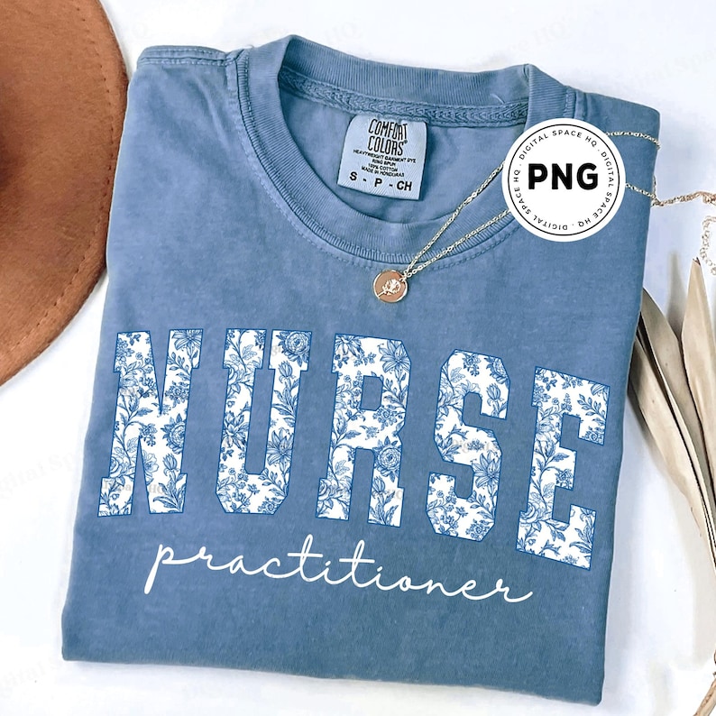 May include: A blue t-shirt with the word "NURSE" in large white floral print letters, and the word "practitioner" in script below. A gold necklace with a pendant is draped on the shirt.