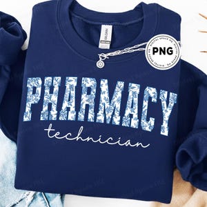 Puede incluir: Una sudadera azul marino con las palabras "PHARMACY technician" en blanco. La palabra "PHARMACY" está rellena con un estampado floral azul. Una cadena plateada con un colgante está drapeada sobre la sudadera.