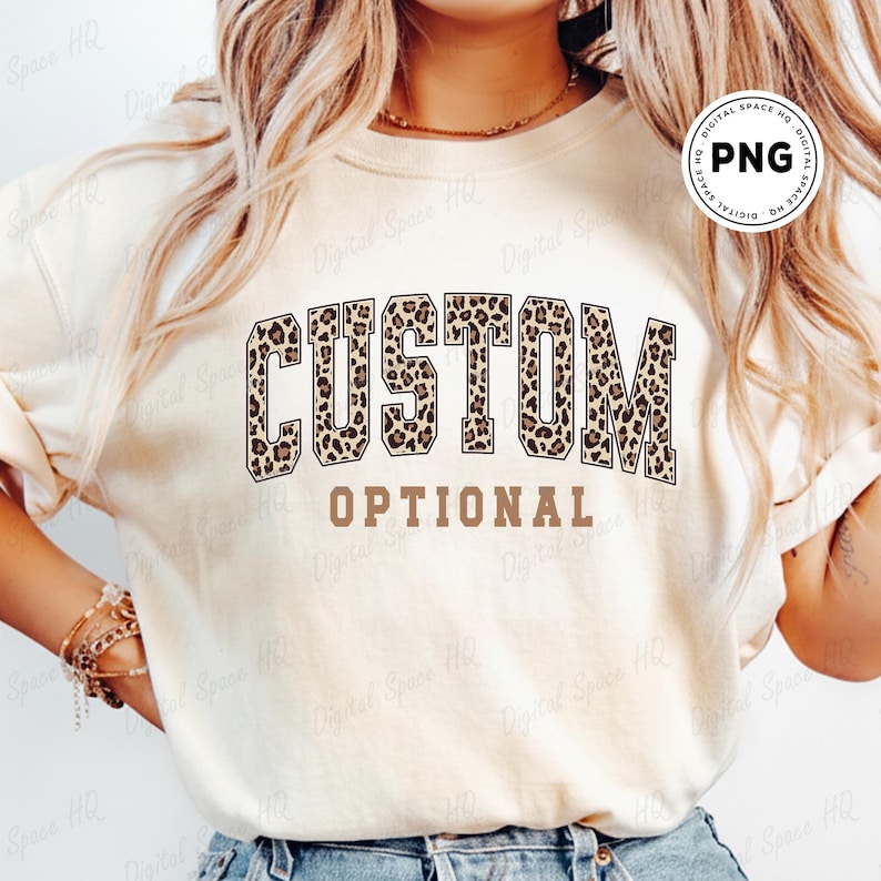 May include: A cream-colored sweatshirt with the words "CUSTOM" in a leopard print design and the word "OPTIONAL" in a brown font. The sweatshirt is a casual style, suitable for everyday wear.
