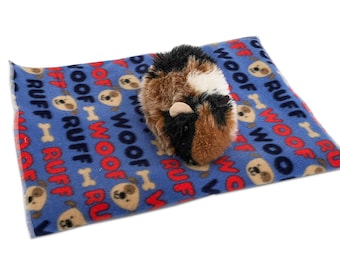 May include: A blue fleece pet bed with a repeating pattern of paw prints and the words "woof" and "ruff" in red. A brown and black guinea pig is lying on the bed.