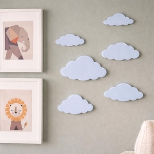 Peut inclure: Décorations murales en forme de nuages bleu clair disposées sur un mur vert clair. Deux tableaux encadrés, représentant un éléphant et un lion, sont également visibles.