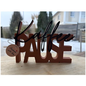 Könnte beinhalten: Ein braunes Holzschild mit den Worten "KAFFEE PAUSE" in einer Mischung aus Block- und Schriftbuchstaben. Das Wort "KAFFEE" ist in schwarzer Schrift, und "PAUSE" ist in Blockbuchstaben. Ein kleines Etikett lautet "Handmade with love."