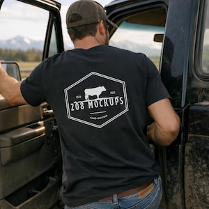 May include: Black t-shirt with a white hexagonal logo on the back. The logo features a cow silhouette, the text "208 MOCKUPS" and "AND GOODS". The shirt is worn by a person near a black truck.