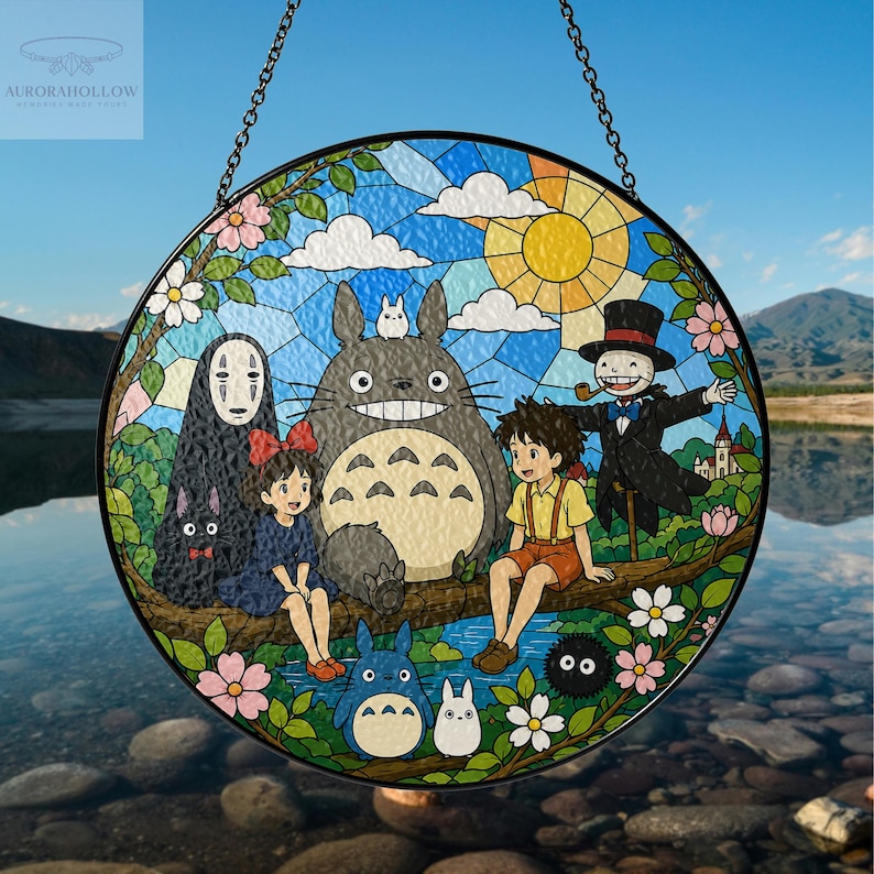 May include: Round stained glass window featuring characters from the animated film "My Neighbor Totoro." The design includes Totoro, other characters, and a sunny sky. The window is framed in black and hangs from a chain.