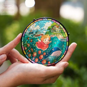 May include: A round stained glass art piece featuring a vibrant illustration of a girl in a red dress, a whale, and boats in the ocean. The artwork is framed with a black border and a colorful edge. The logo "AURORAHOLLOW" is in the upper left corner.
