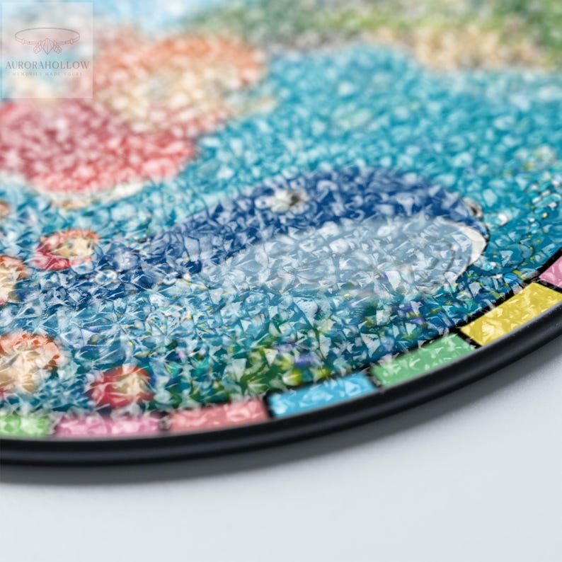 May include: Close-up of a round, mosaic-style decorative piece with a black border. The mosaic features a colorful design with shades of blue, red, orange, and green. The image includes the text "AURORAHOLLOW" in the upper left corner.