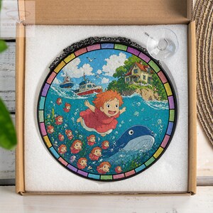May include: Round stained glass art featuring a vibrant scene with a red-haired character, a whale, and boats on the ocean. The artwork is framed with a black metal chain and a rainbow-colored border. Includes a suction cup for hanging.