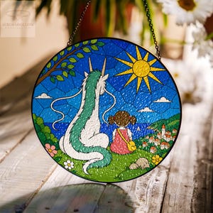 May include: Round stained glass window art featuring a scene from a popular animated film. The artwork depicts a girl and a dragon-like creature overlooking a coastal town. The sky is blue with a yellow sun, and the piece is framed with a black metal chain.