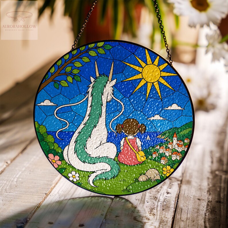 May include: Round stained glass window art featuring a scene from a popular animated film. The artwork depicts a girl and a dragon-like creature overlooking a coastal town. The sky is blue with a yellow sun, and the piece is framed with a black metal chain.