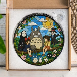 May include: Round stained glass panel featuring a colorful illustration of characters from the animated film "My Neighbor Totoro." The artwork depicts Totoro, Mei, Satsuki, and other characters in a vibrant outdoor scene with a blue sky and yellow sun.