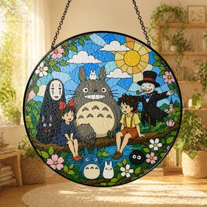 May include: A round stained glass panel featuring characters from the animated film "My Neighbor Totoro." The design includes Totoro, a cat bus, and other characters, set against a blue sky with a yellow sun and white clouds. The panel is framed with a black border and a hanging chain.