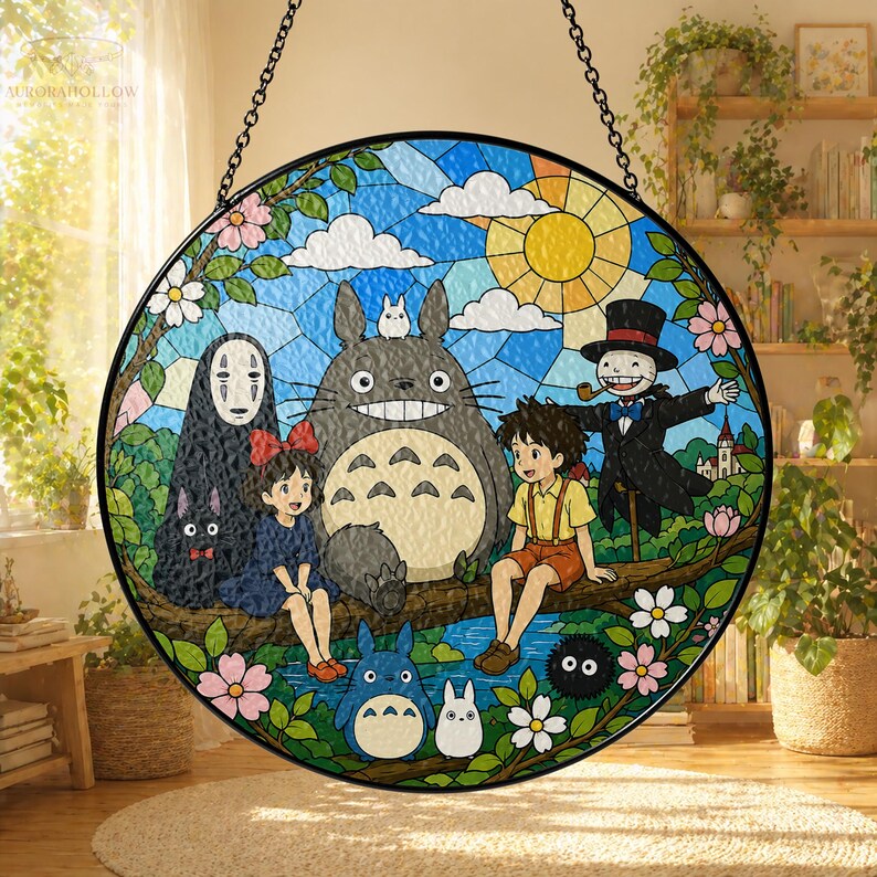 May include: A round stained glass panel featuring characters from the animated film "My Neighbor Totoro." The design includes Totoro, a cat bus, and other characters, set against a blue sky with a yellow sun and white clouds. The panel is framed with a black border and a hanging chain.