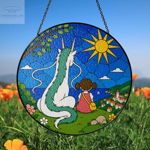 May include: Round stained glass window art featuring a scene with a white and green dragon, a girl in a red dress, and a coastal village under a bright yellow sun. The artwork is framed in black and hangs from a chain.