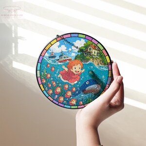 May include: A round, colorful stained-glass art piece featuring a vibrant illustration of a girl in a red dress swimming in the ocean with a blue fish. Boats and a house are visible in the background. The piece is held by a hand.