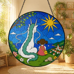 May include: Round stained glass window art featuring a dragon and a girl overlooking a coastal town. The artwork has a blue sky with a yellow sun, green grass, and colorful flowers. The piece is suspended by a black chain.