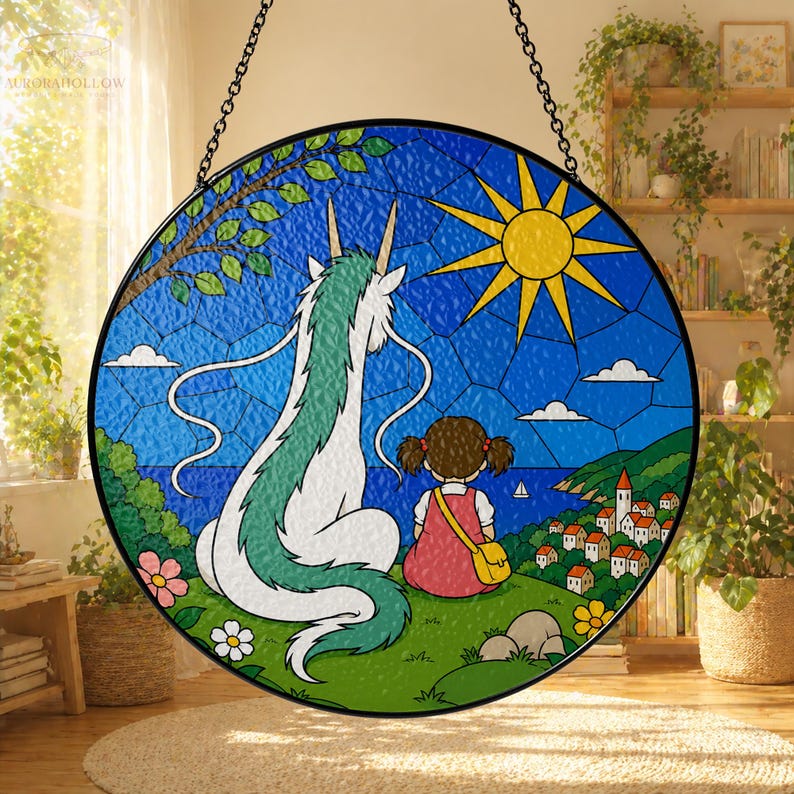 May include: Round stained glass window art featuring a dragon and a girl overlooking a coastal town. The artwork has a blue sky with a yellow sun, green grass, and colorful flowers. The piece is suspended by a black chain.