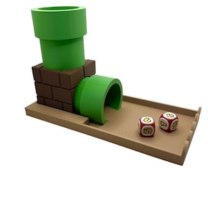 May include: A green and brown 3D-printed game piece resembling a Super Mario Bros. warp pipe. The set includes two red dice with yellow and white markings, all on a tan tray.