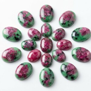 May include: A collection of fifteen oval-shaped cabochons arranged in a circular pattern. Each stone features a polished surface with a distinct mottled appearance, combining vibrant magenta-pink inclusions with deep green and black mineral matrix.