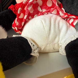 May include: A plush doll featuring a red and white polka dot dress, white bloomers with lace trim, and black legs. The doll's dress is ruffled, and the bloomers have delicate lace detailing. The doll is a classic character.