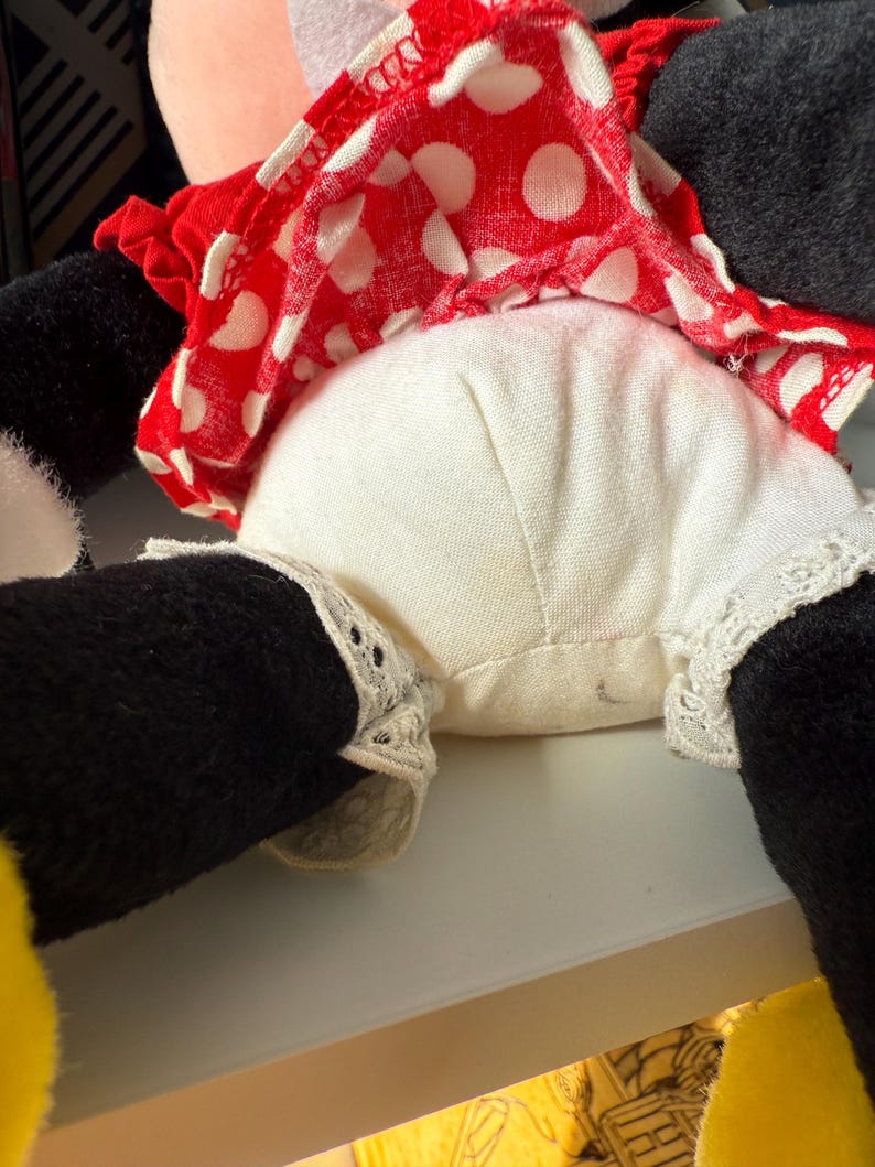 May include: A plush doll featuring a red and white polka dot dress, white bloomers with lace trim, and black legs. The doll's dress is ruffled, and the bloomers have delicate lace detailing. The doll is a classic character.