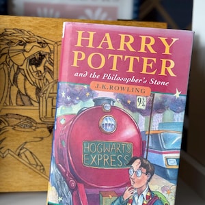 May include: A first edition of "Harry Potter and the Philosopher's Stone" by J.K. Rowling. The book cover shows a red Hogwarts Express train, a young boy with glasses, and the words "Hogwarts Express". The book is a winner of the 1997 Smarties Gold Award.
