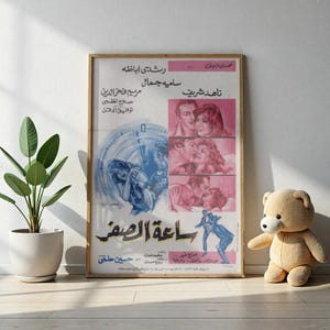 Puede incluir: Un póster de película vintage enmarcado con texto árabe e imágenes de actores. El póster tiene una combinación de colores rosa y azul, con el título "Saa'at Al-Sifr" en un lugar destacado. El póster está en un marco de madera.