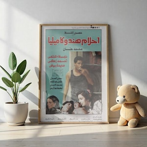 Puede incluir: Un póster de película vintage enmarcado con texto árabe e imágenes de actores. El póster está en un marco de madera y se apoya contra una pared blanca. Una planta en maceta y un oso de peluche están al lado del póster.