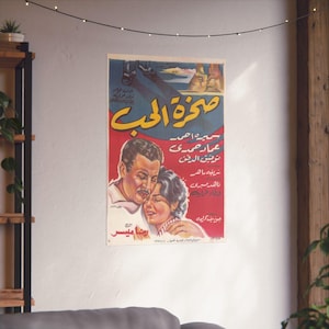 May include: A vintage movie poster with Arabic text and imagery. The poster features a couple embracing, set against a backdrop of a desert landscape. The color palette includes red, yellow, blue, and white.