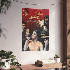 Può includere: Un poster cinematografico vintage con sfondo rosso e immagini di attori. Il poster presenta testo arabo e la frase inglese "Silence... on tourne". Una donna in abito giallo tiene un microfono. Il poster è su un muro bianco.