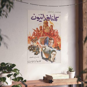 Puede incluir: Un cartel de película vintage con texto árabe e ilustraciones de figuras armadas, un jeep y llamas. El cartel está montado en una pared blanca, con una estantería de madera y plantas en primer plano.