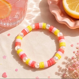 May include: A circular bracelet composed of alternating white faux pearl beads and flat, disc-shaped polymer clay beads in vibrant shades of yellow, light pink, and coral orange, arranged in a repeating pattern around the entire circumference.