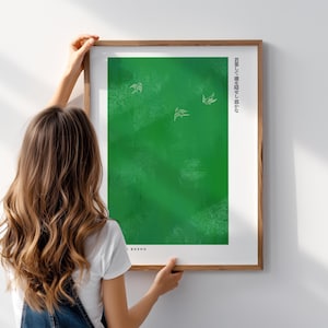 Puede incluir: Una impresión artística enmarcada con un fondo verde y tres ilustraciones de pájaros blancos. Texto japonés impreso verticalmente a la derecha. La impresión es sostenida por una persona.